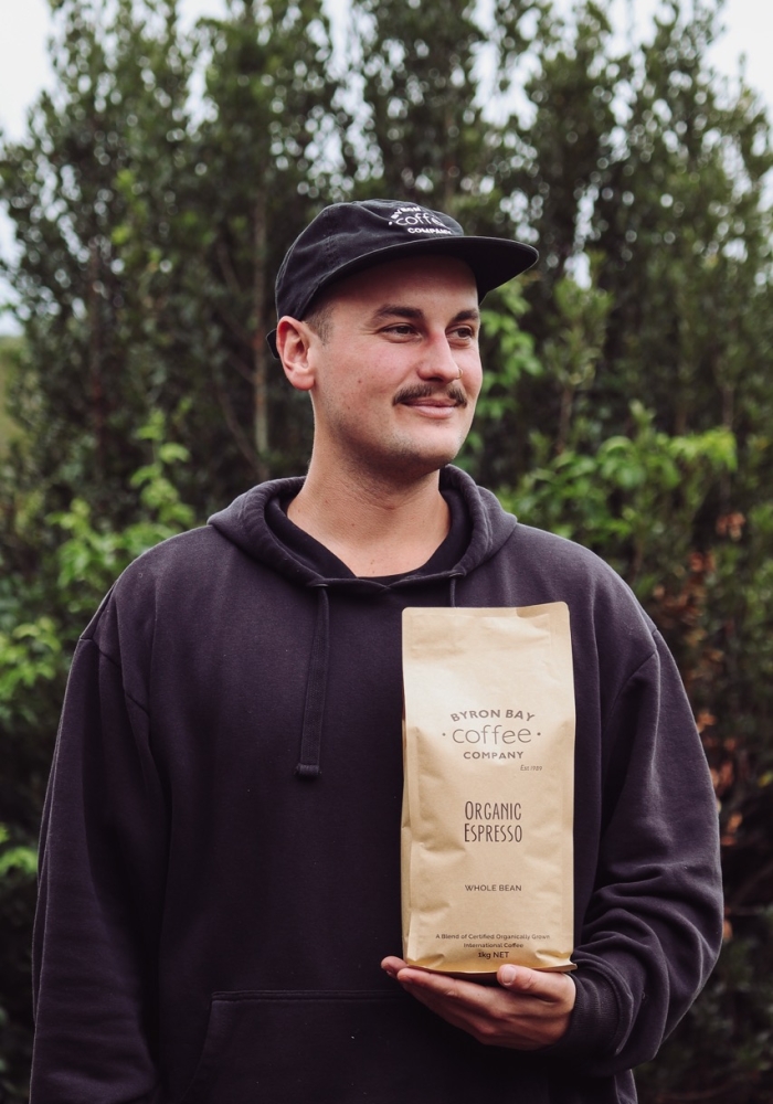 Man Holding Organic Coffee Kilo Pack Wearing a Byron Bay Coffee Company Cap