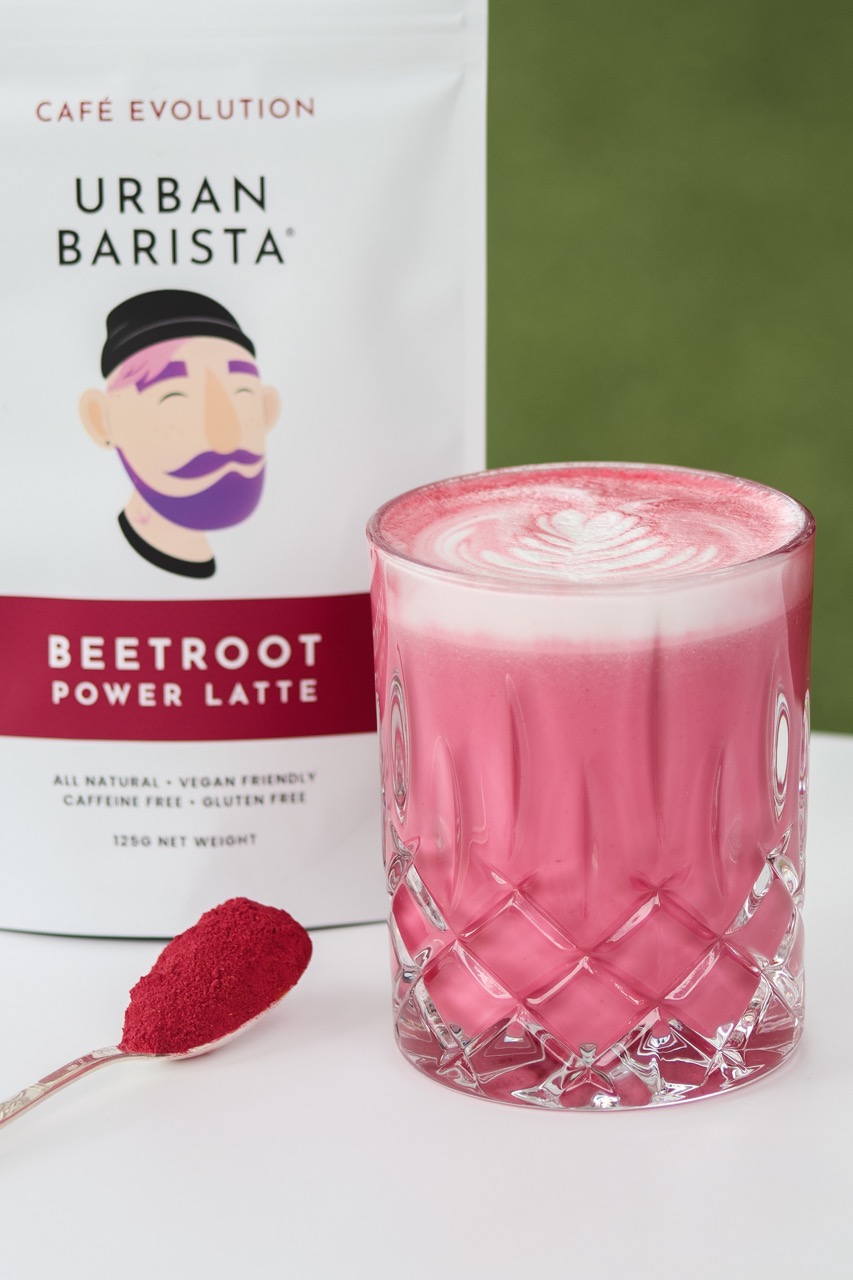 Beetroot latte in a glass next to a pouch of Urban Barista matcha latte mix