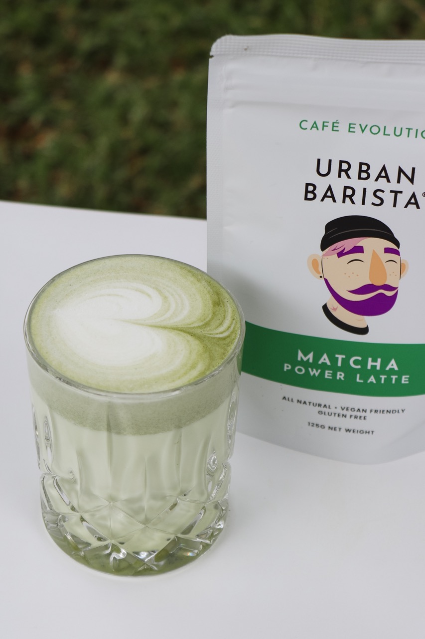 Matcha latte in a glass next to a pouch of Urban Barista matcha latte mix